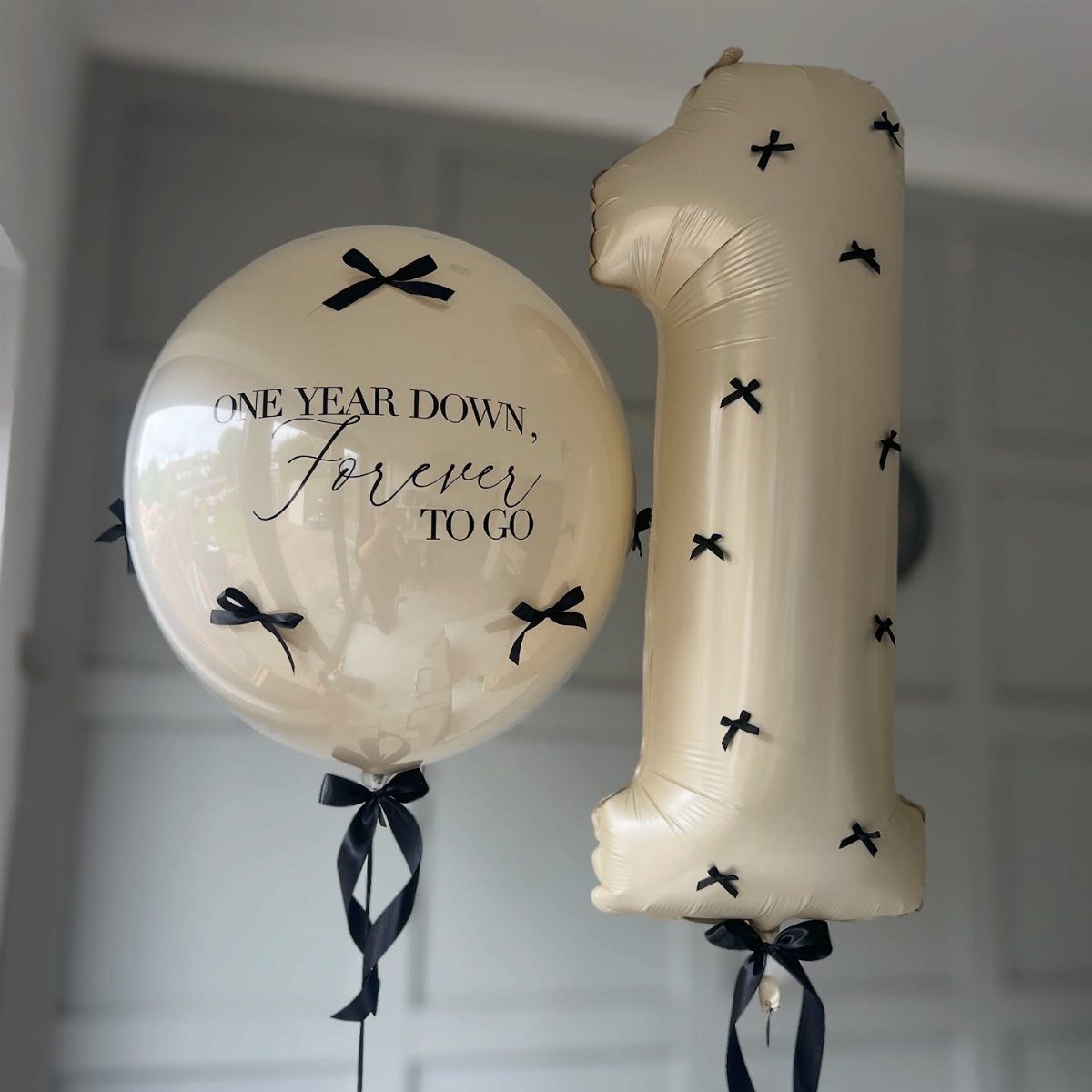 Cream-colored balloons including a giant number one and a sphere with romantic text.