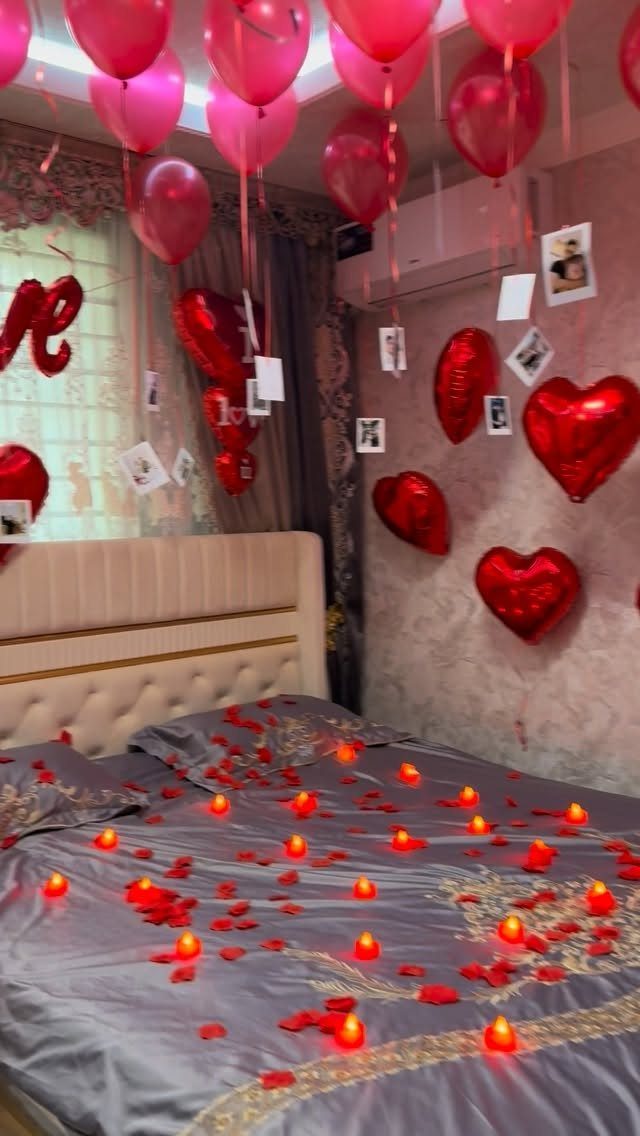 Red heart balloons and round balloons decorating a bedroom with rose petals and candles.