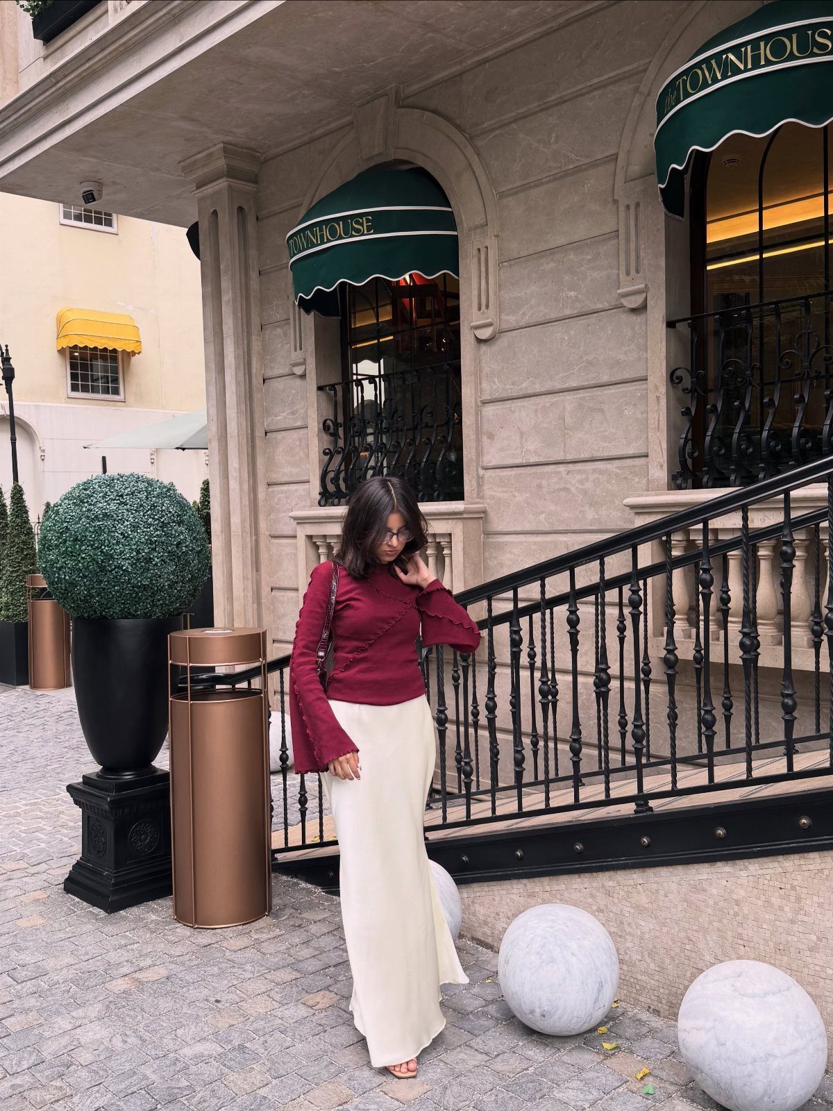Woman wearing a maroon flared-sleeve top and long cream skirt standing outdoors.