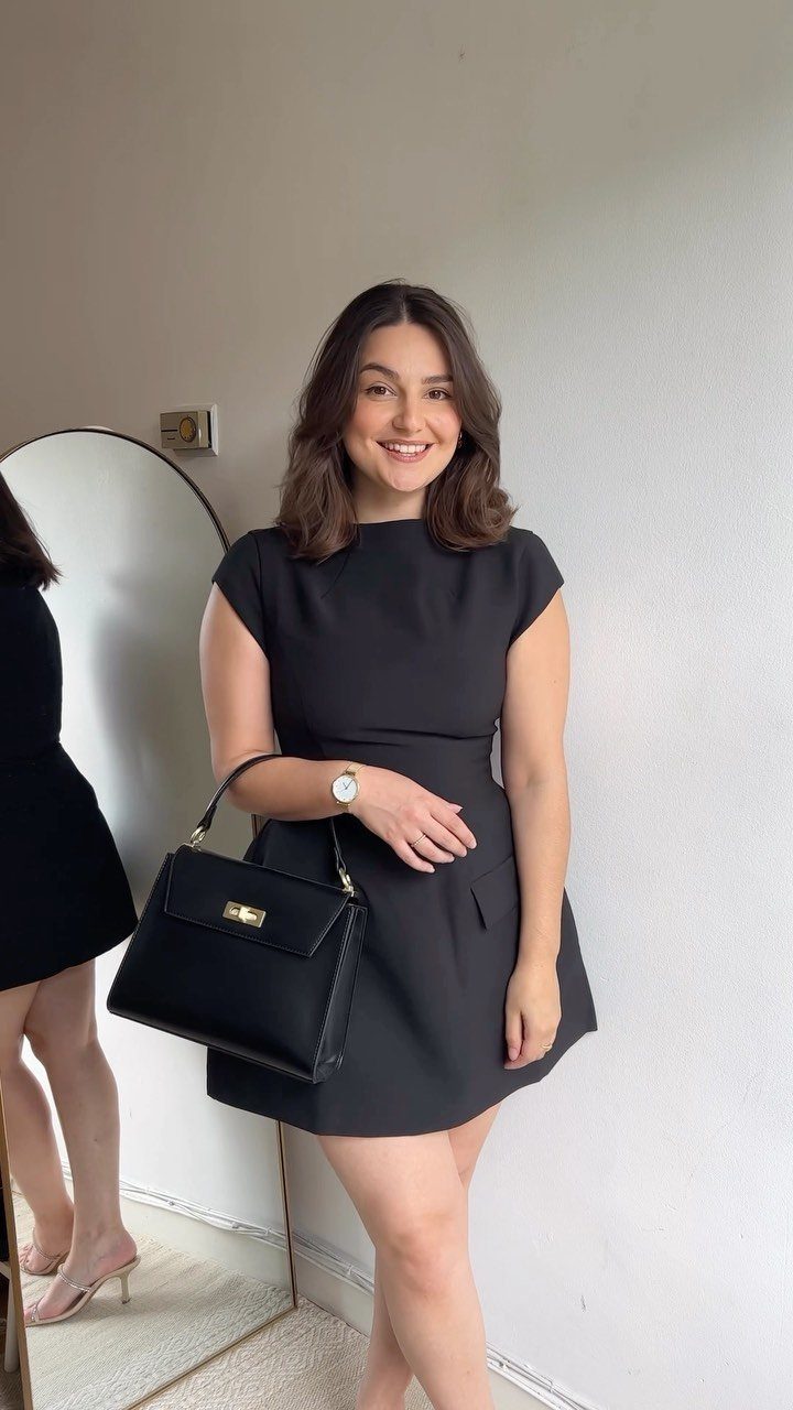 Woman wearing a short sleeveless black dress and holding a black handbag.