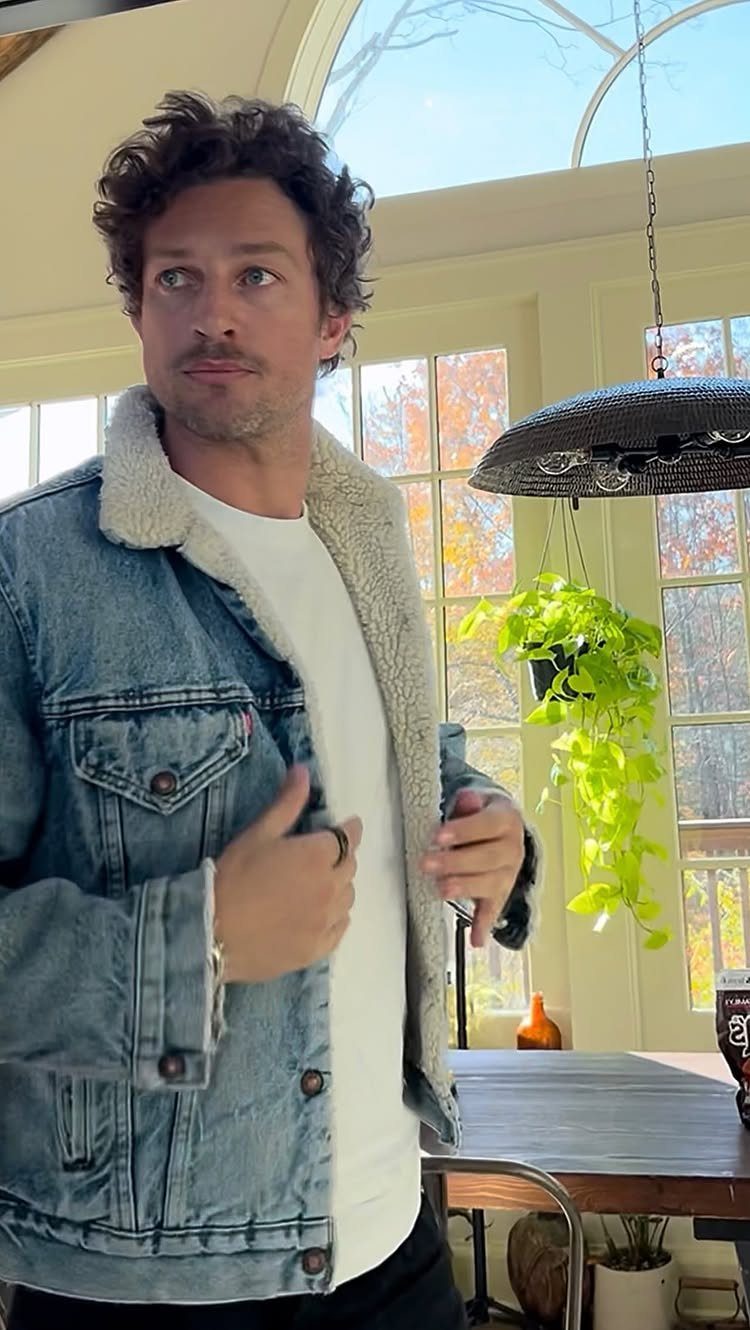 Man wearing a white t-shirt and a sherpa-lined denim jacket indoors.