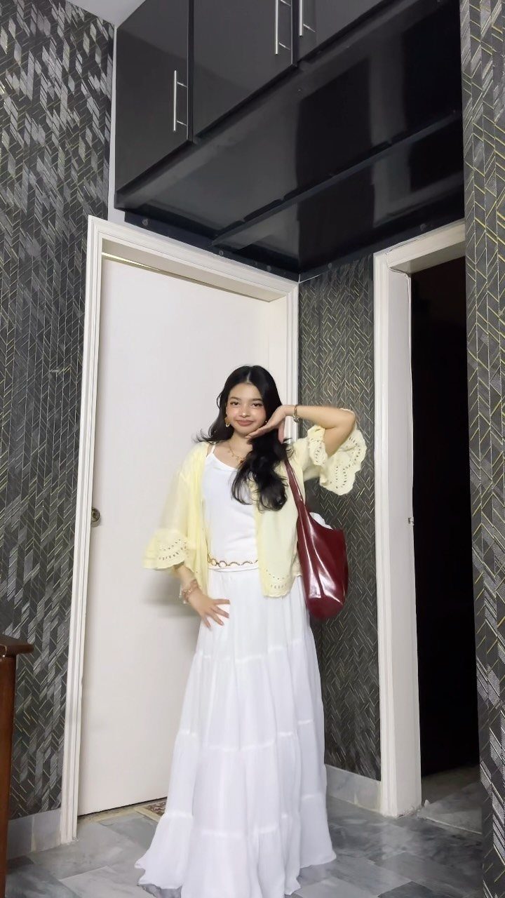 Woman in a white tiered dress and yellow cardigan carrying a red handbag.