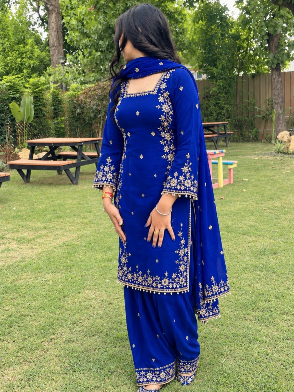Woman wearing a royal blue embroidered Salwar Kameez standing in a green backyard