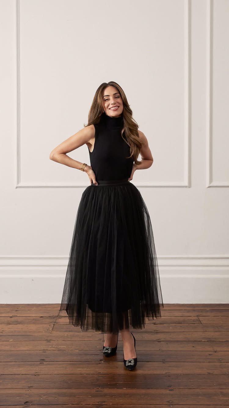 Woman wearing a black high-neck top and a voluminous black tulle midi skirt.