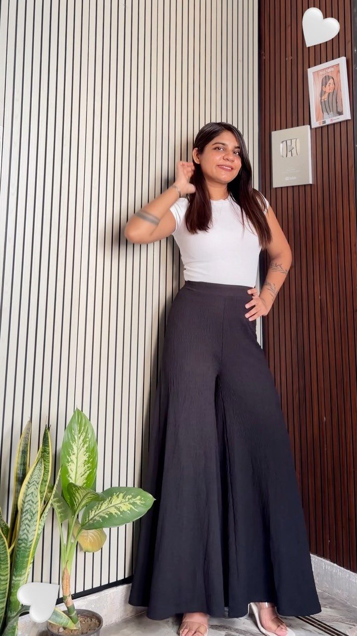 Woman wearing a white sleeveless top and high-waisted black wide-leg trousers posing indoors.