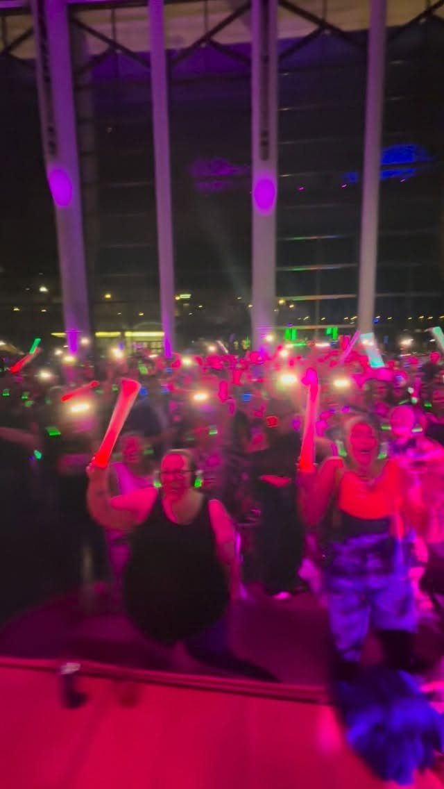 Crowd of people holding glowing neon sticks at a dark party venue.