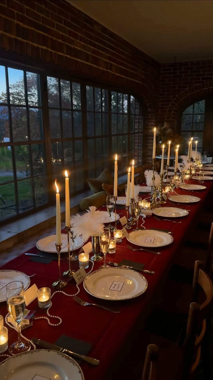 Elegant dinner table set with red cloth, white plates, and many lit candles.