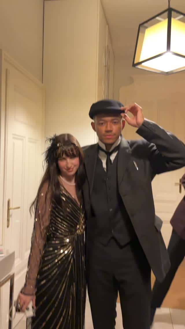 Man in a vintage suit and woman in a sequined dress posing indoors.