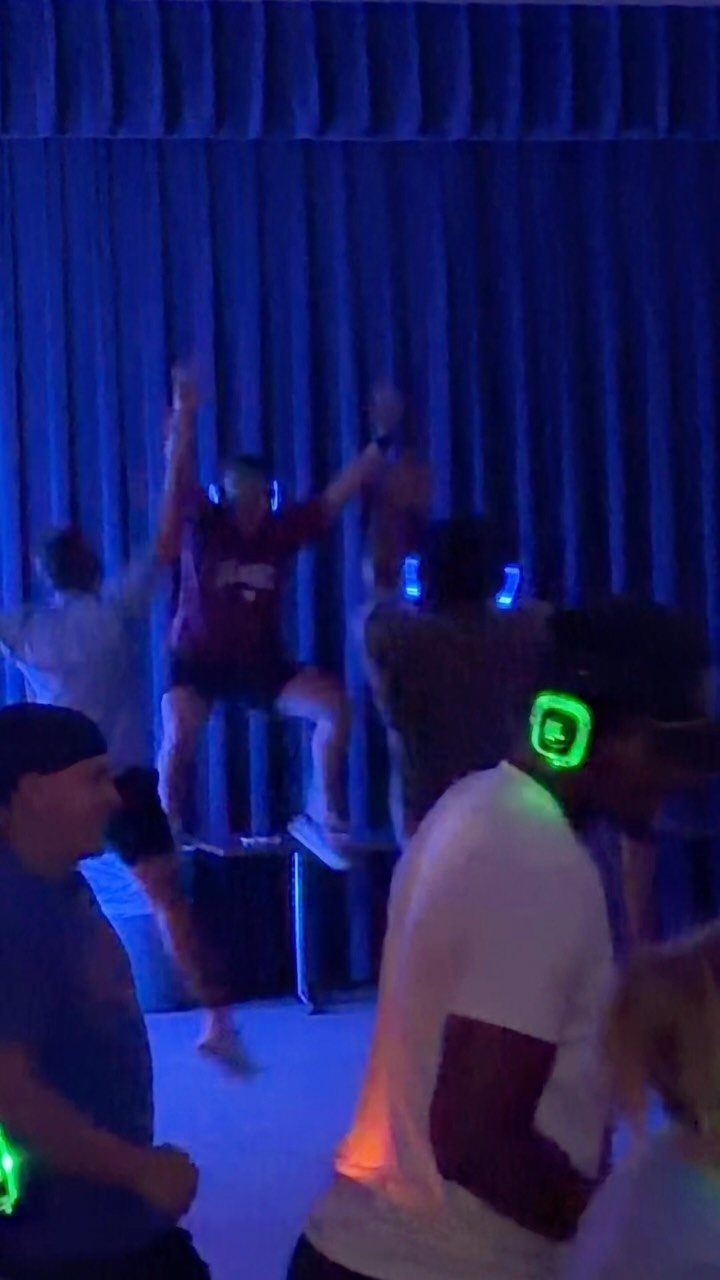 People dancing in a blue-lit room wearing glowing green wireless headphones.