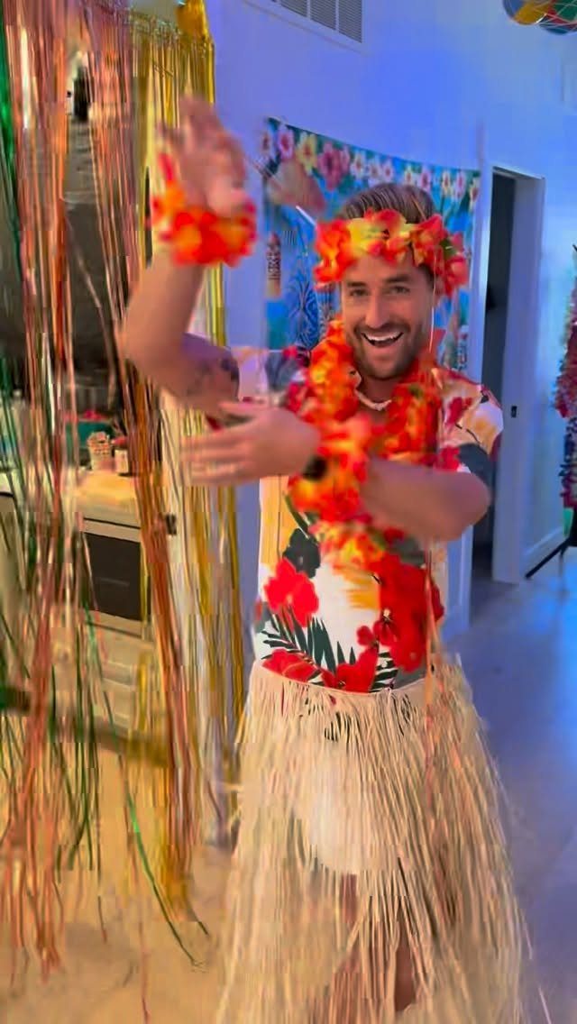 Man in Hawaiian shirt and hula skirt wearing floral leis at a party