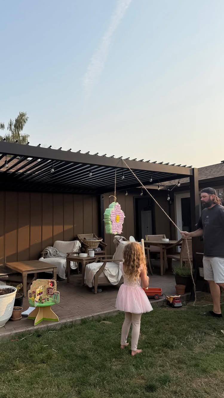 Young girl in pink tutu looking at a colorful piñata in a backyard.