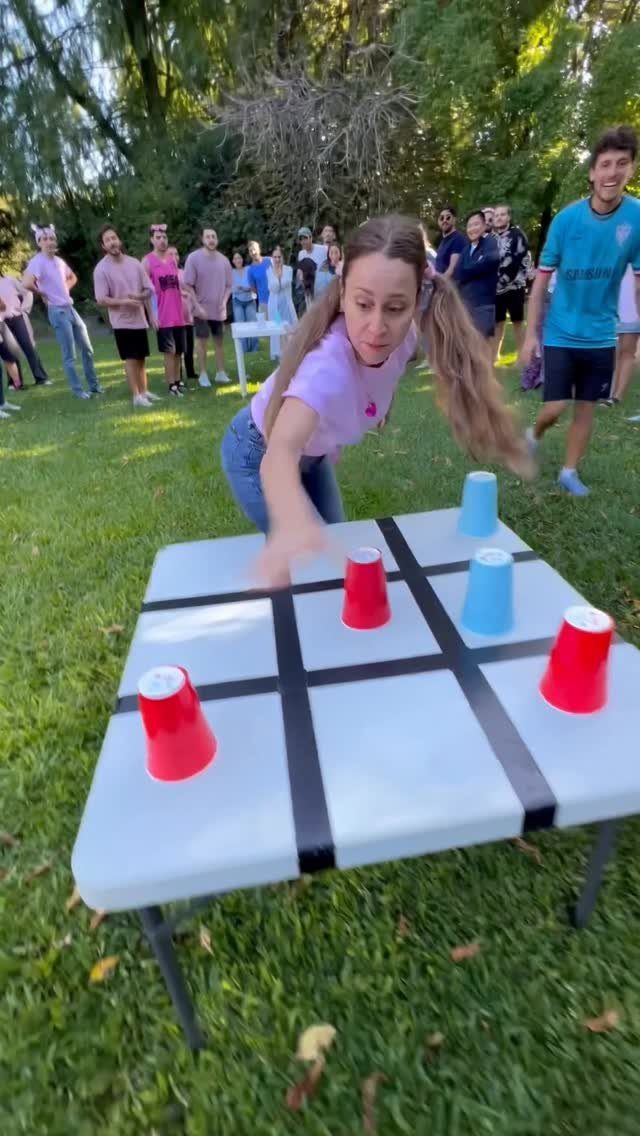 Woman playing giant tic-tac-toe with red and blue cups on a white table outdoors.