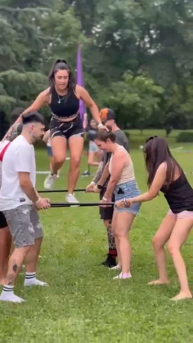 Young adults playing a jumping game with elastic bands on a grassy lawn