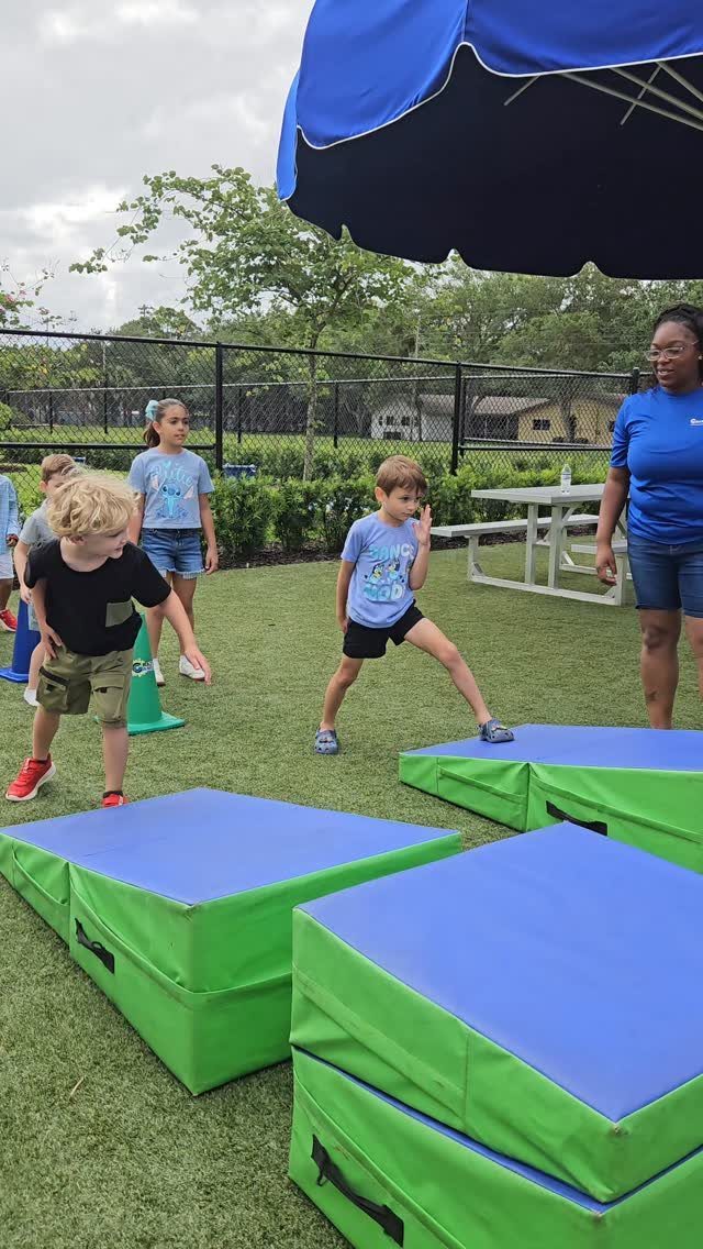 Children jumping on colorful foam pads during an outdoor party activity on grass.