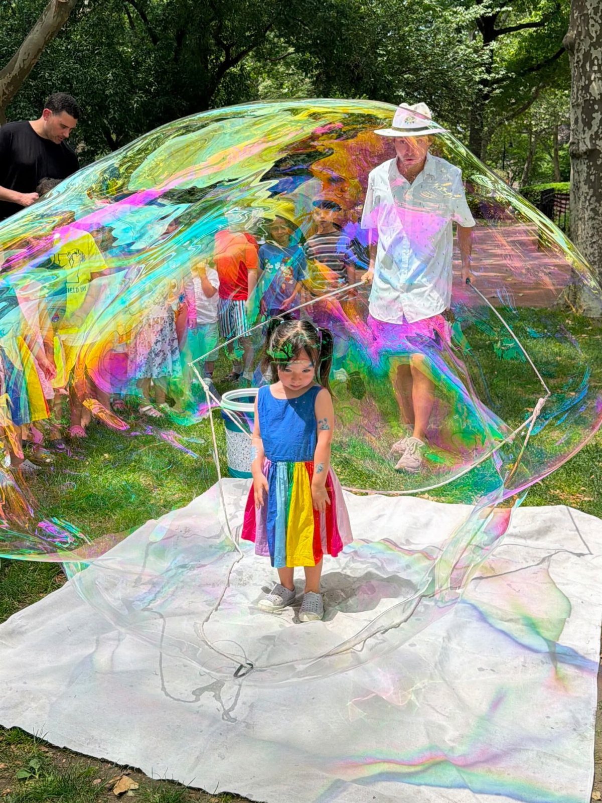 Young girl standing inside a massive iridescent soap bubble in a grassy park.