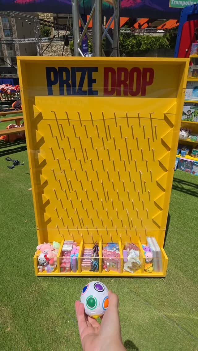 Yellow prize drop game board with toys on grass, held colorful ball