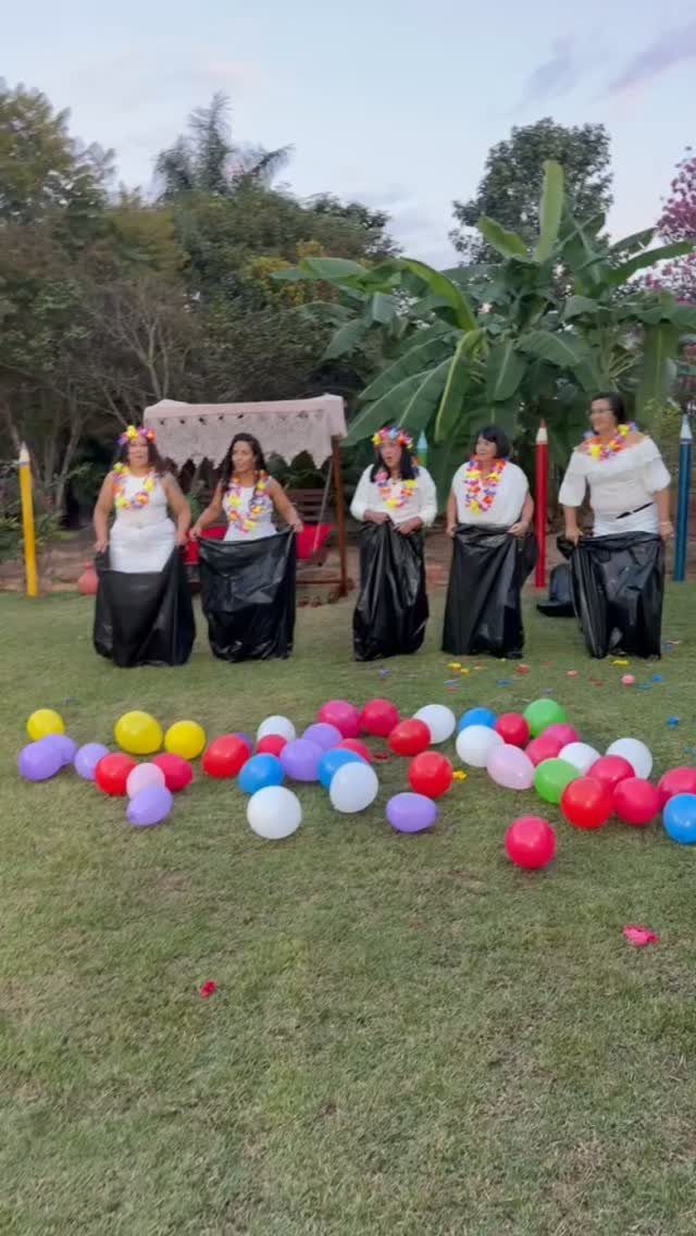 Five women in black trash bags playing a game with colorful balloons outdoors