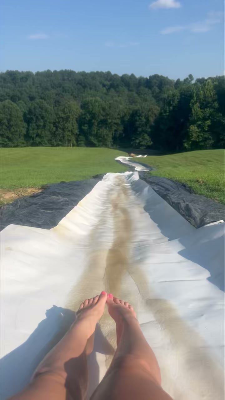 Long white plastic slip 'n slide on a green lawn leading toward trees.
