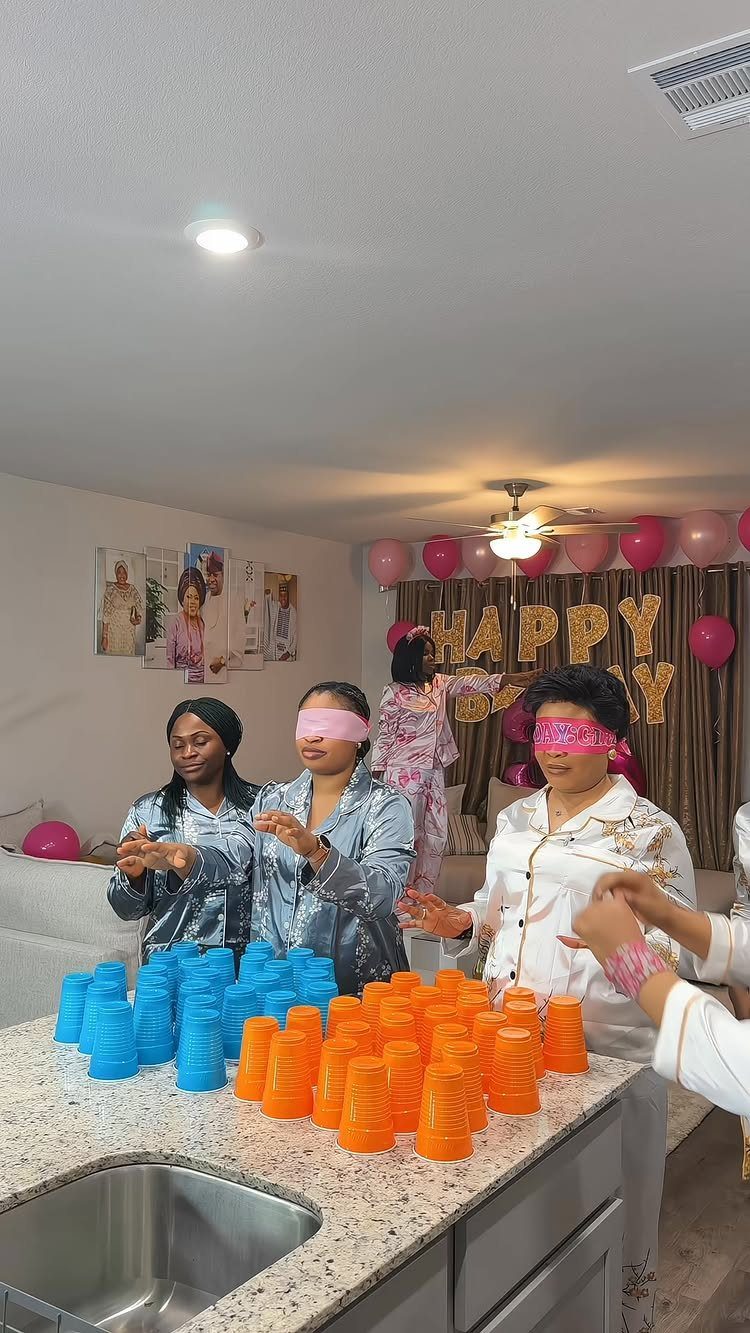 Women in pajamas playing a blindfolded cup stacking game at a birthday party.