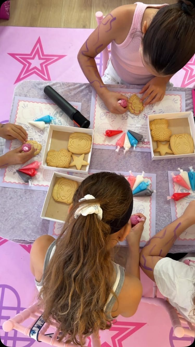Children decorating star and square cookies with colorful frosting at a party table.