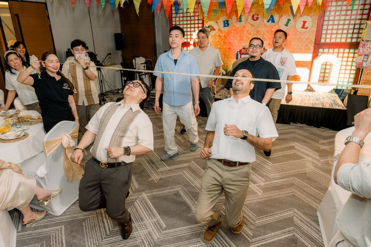 Men leaning backward to pass under a limbo stick at a party.