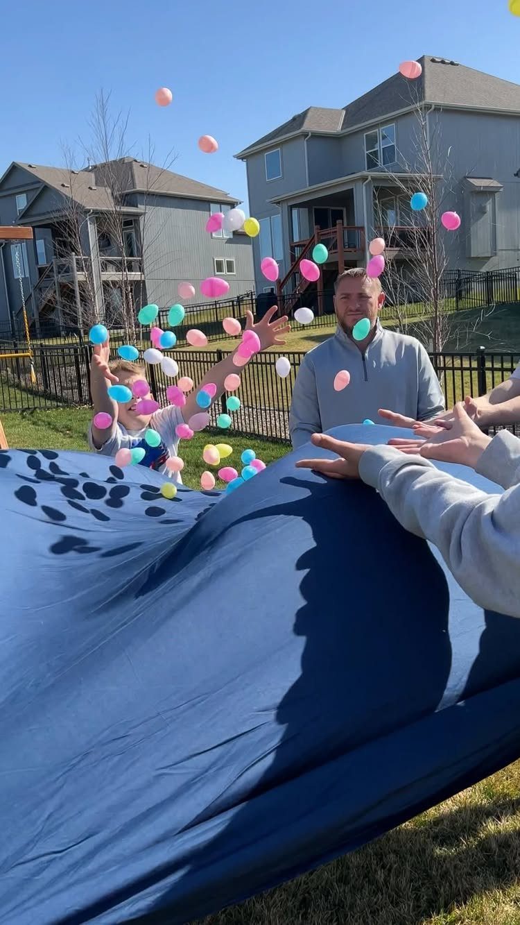 Man and child tossing colorful balloons into the air with a blue sheet.