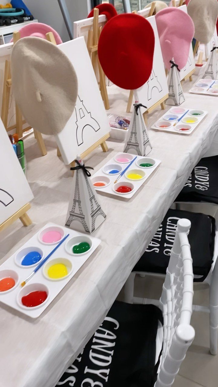 Painting station with small easels, colorful paint palettes, and berets on a table.