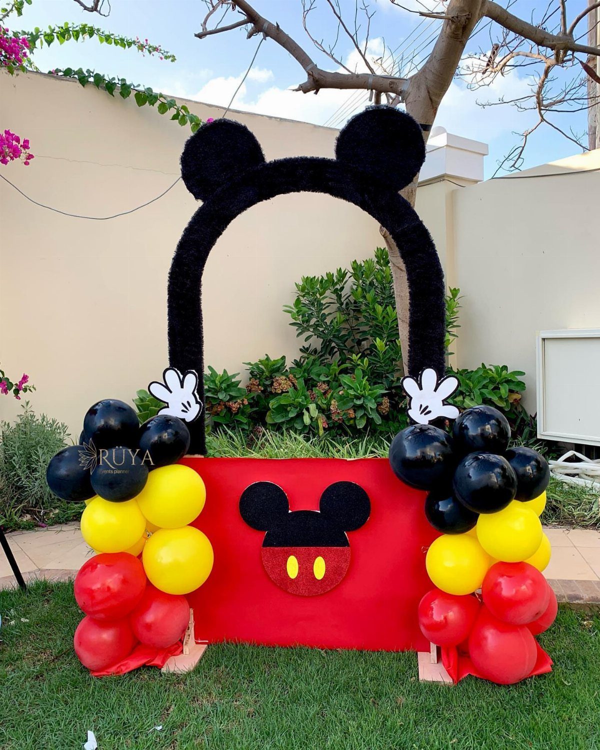 Mickey Mouse themed photo booth backdrop with balloons on a green lawn