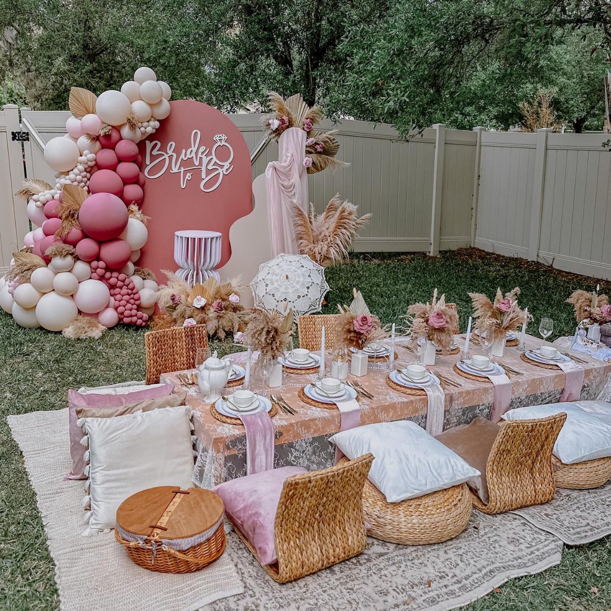 Low outdoor table with pink linens, white plates, and a bridal balloon arch.