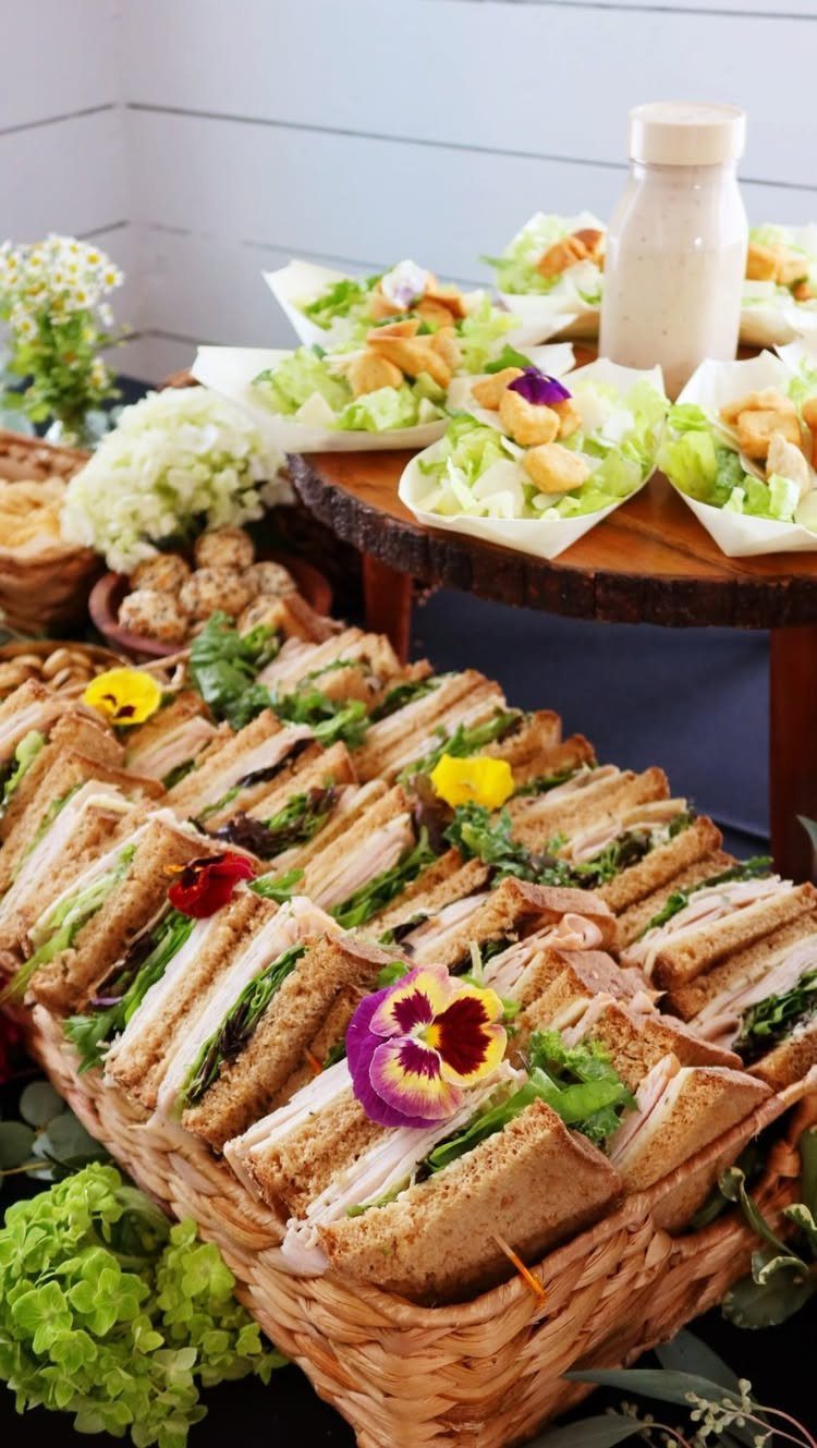 Small sandwiches with edible flowers in a woven basket at a brunch buffet.