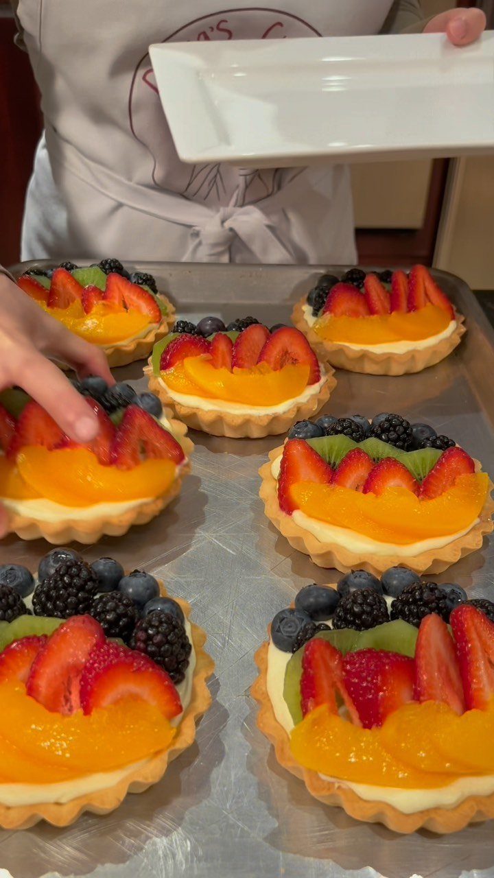 Fruit tarts with strawberries, peaches, and berries on a metal baking sheet.