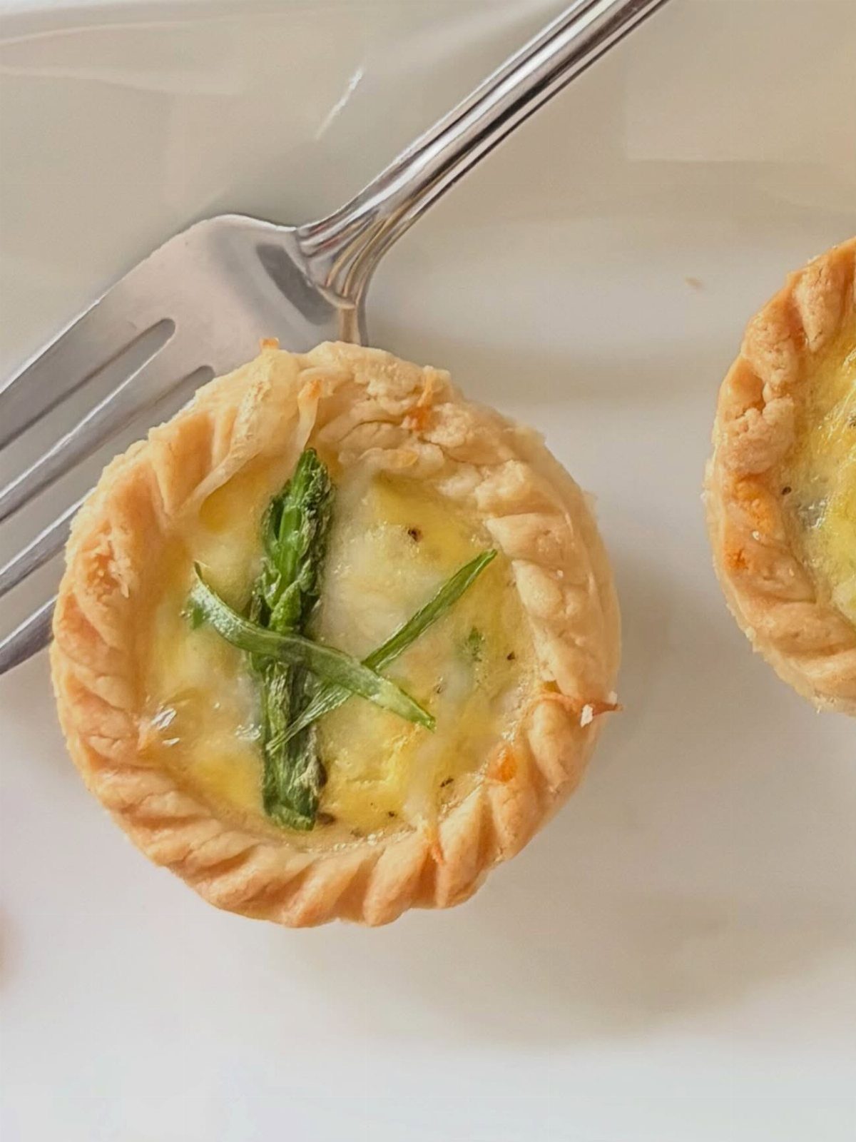 Mini quiches with asparagus on a white plate with a silver fork.