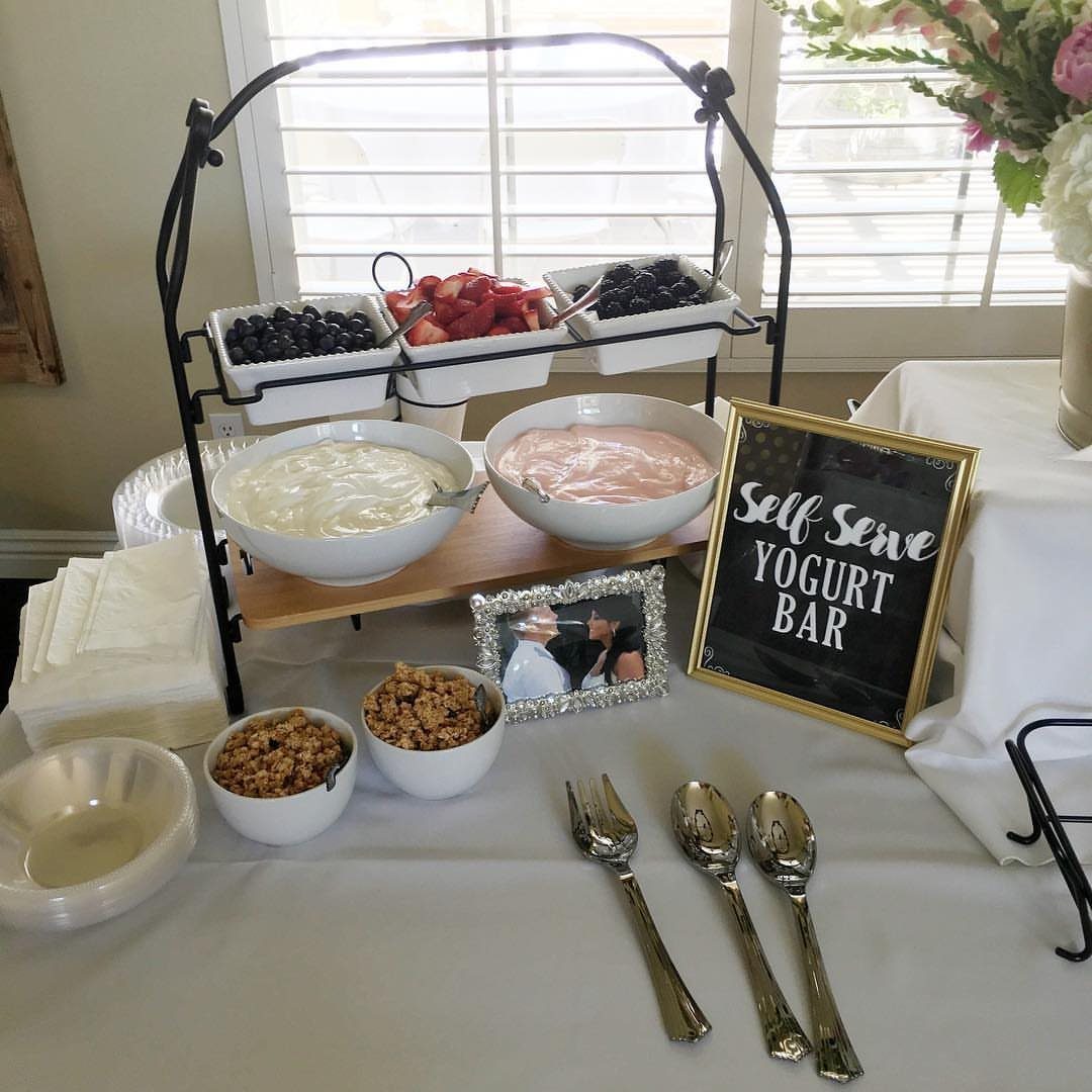 Yogurt bar setup with bowls of yogurt, fresh berries, granola, and a chalkboard sign.