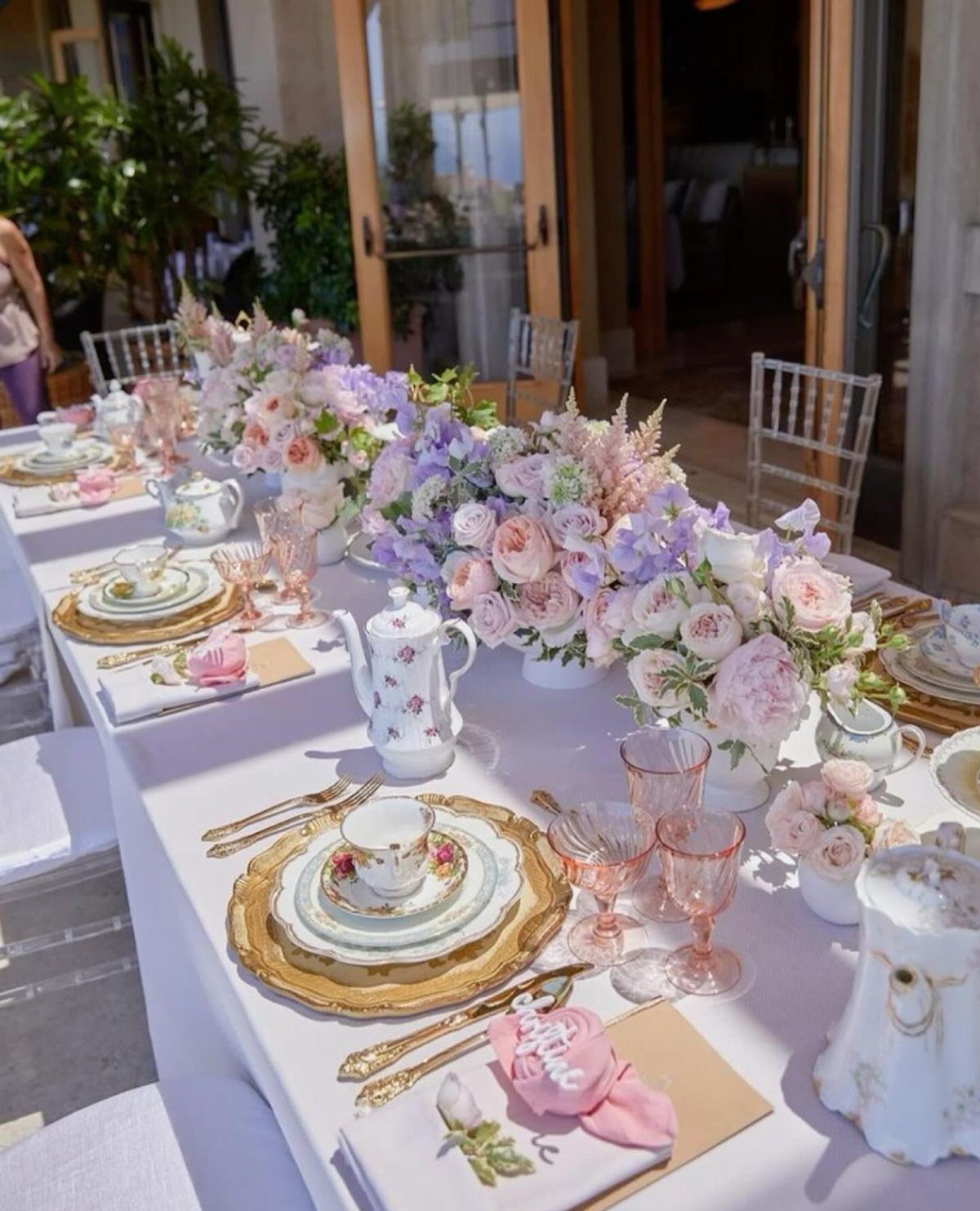 Elegant table setting with pink roses, white teapots, and gold plates for tea.