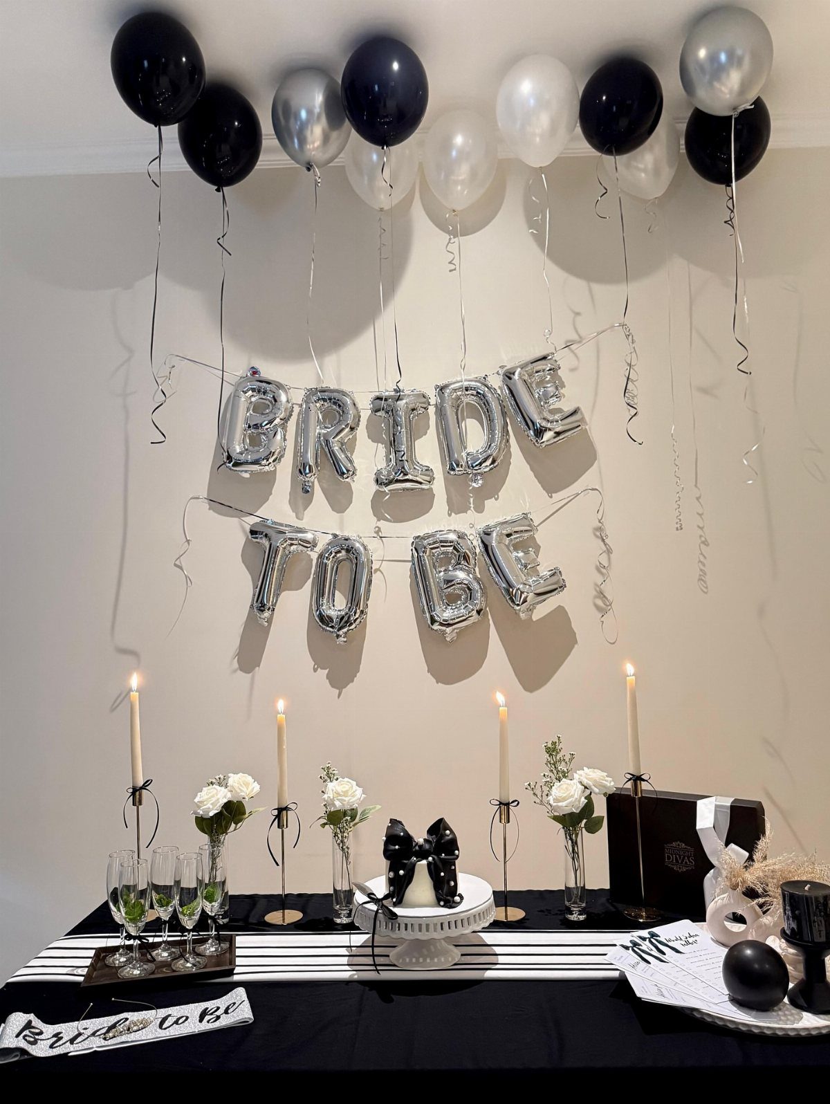 Bridal shower table with black and white decor, silver balloons, and white flowers.