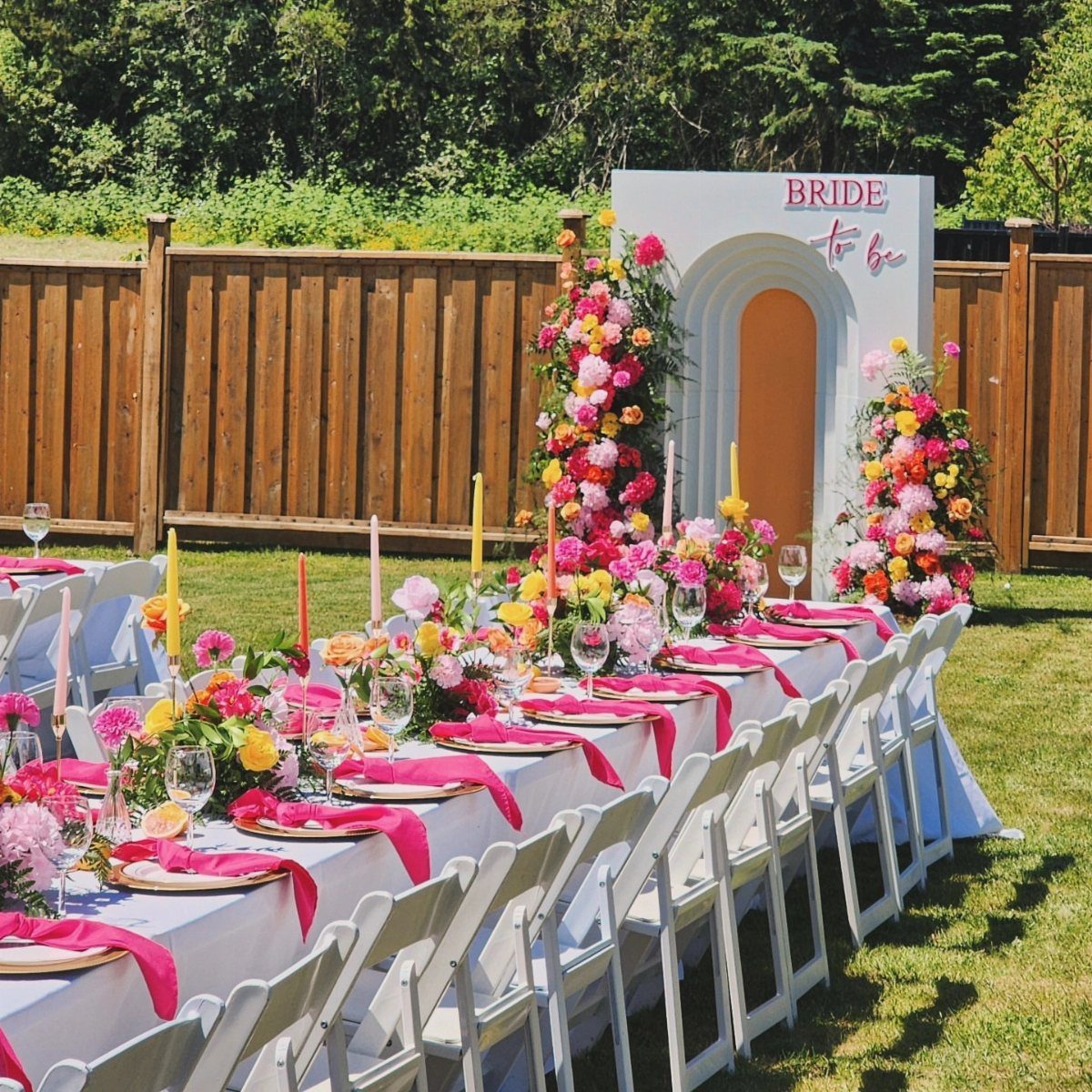Outdoor bridal shower table with pink napkins and colorful floral centerpieces and backdrop