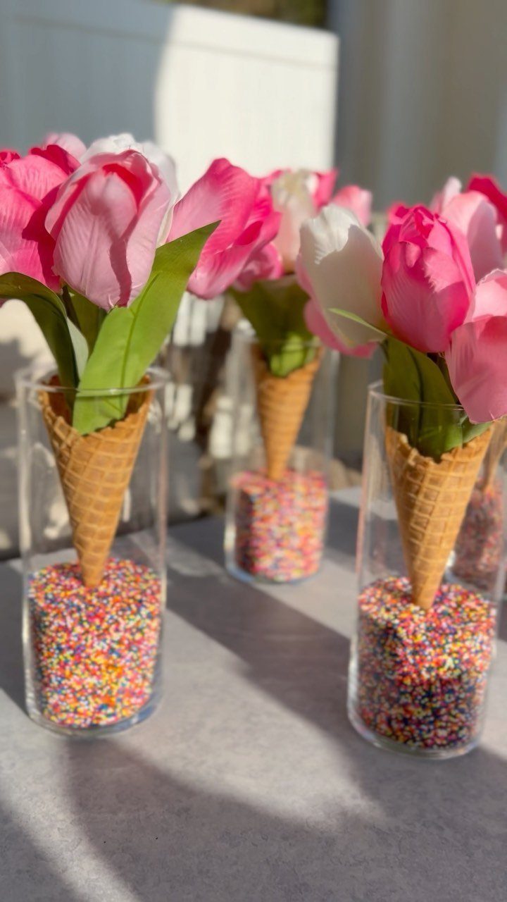 Pink and white tulips in waffle cones placed inside sprinkle-filled glass cylinders.