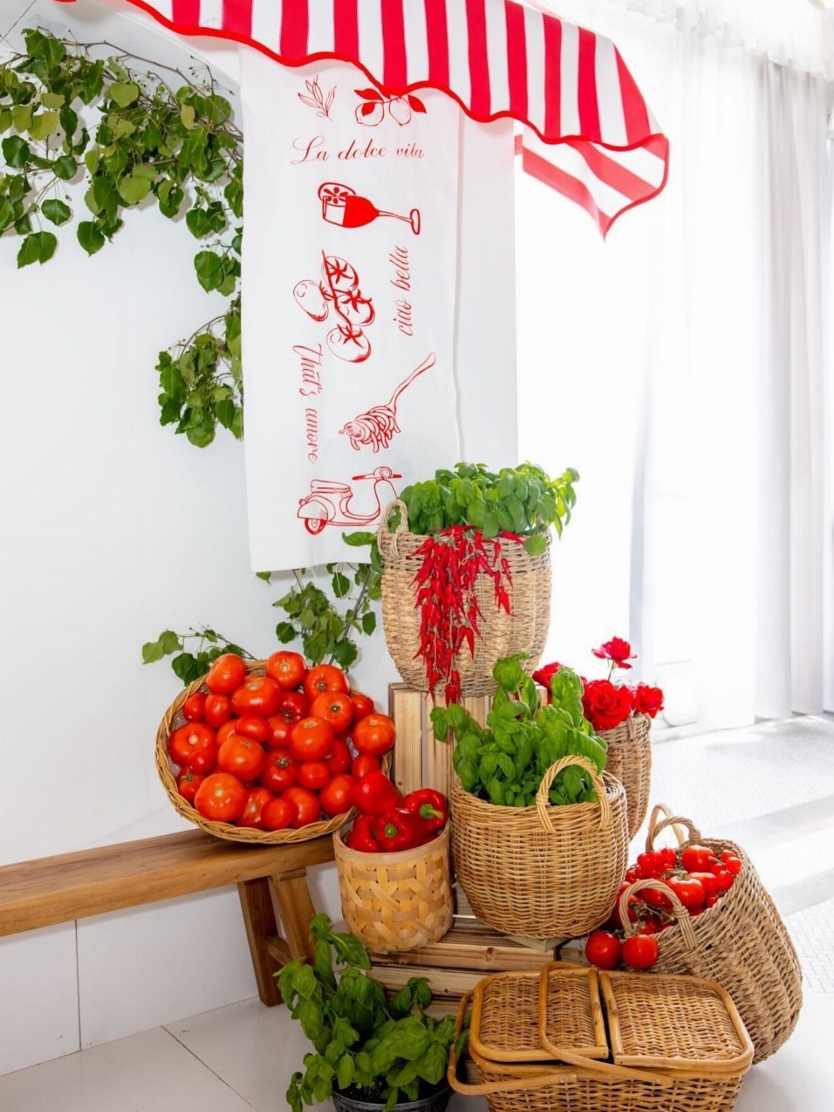 Baskets of fresh tomatoes, chilies, and basil under a red striped awning.