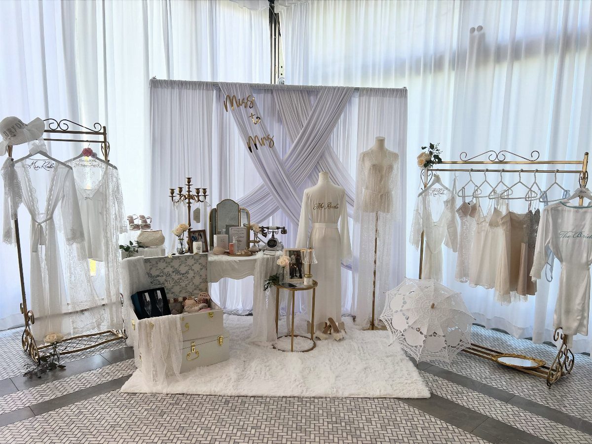 White lace robes and lingerie displayed on gold racks in a bridal setup.