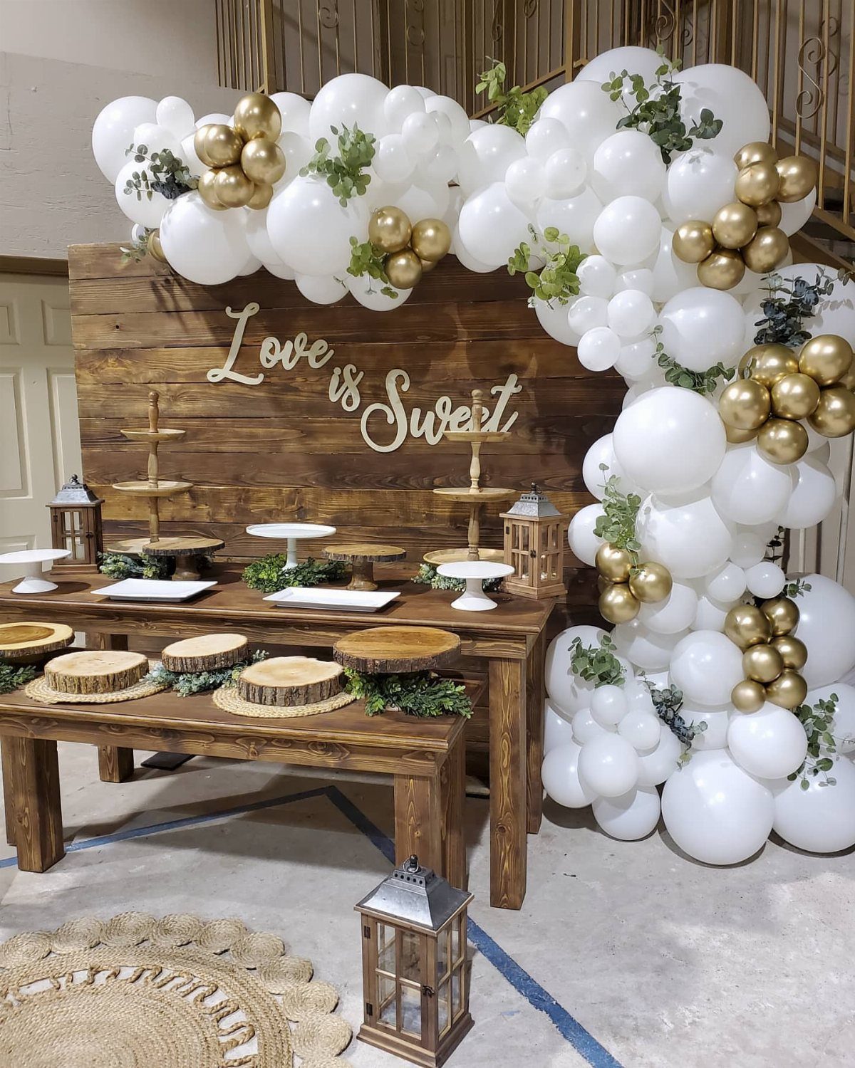 Wooden dessert table with white and gold balloon arch and Love is Sweet sign