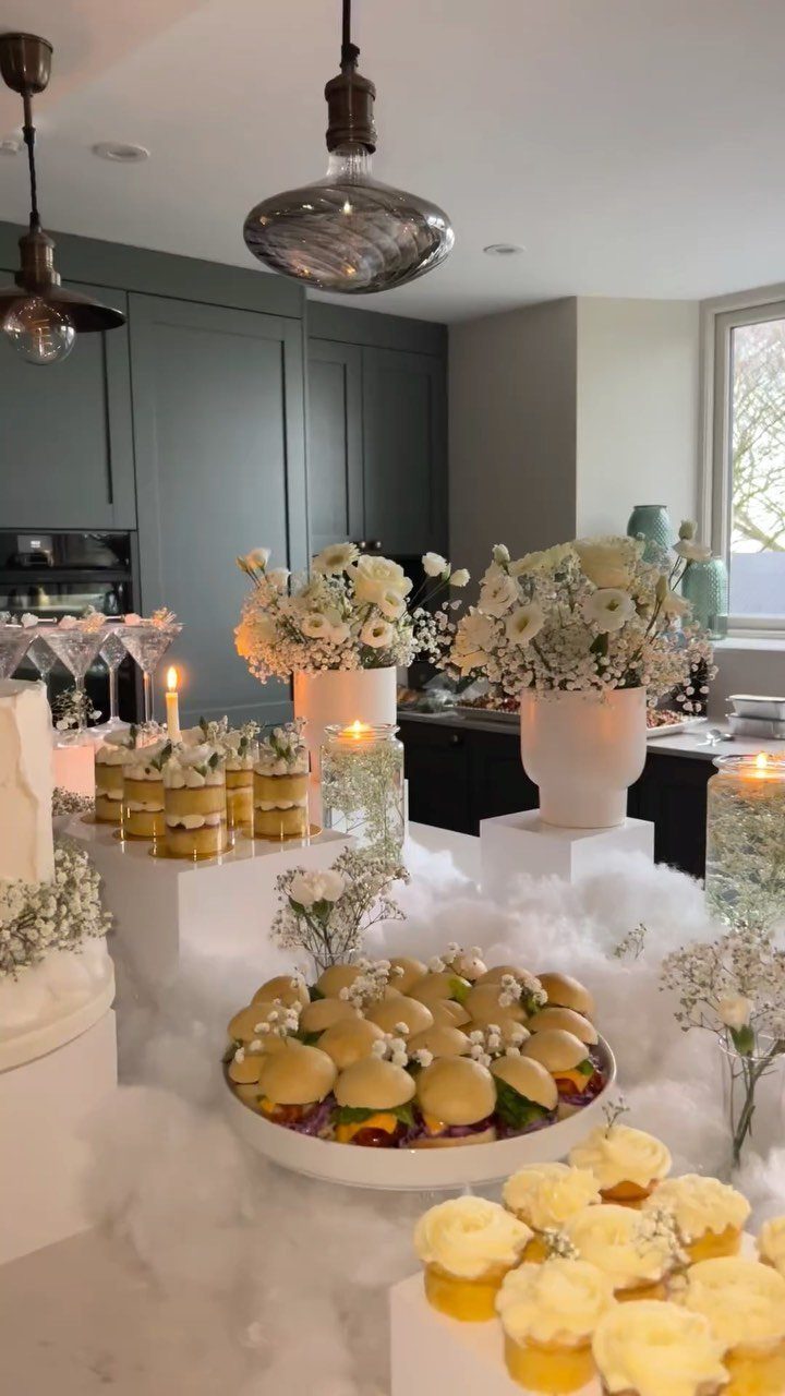 Dessert table with white flowers and food surrounded by fluffy white cloud decor.