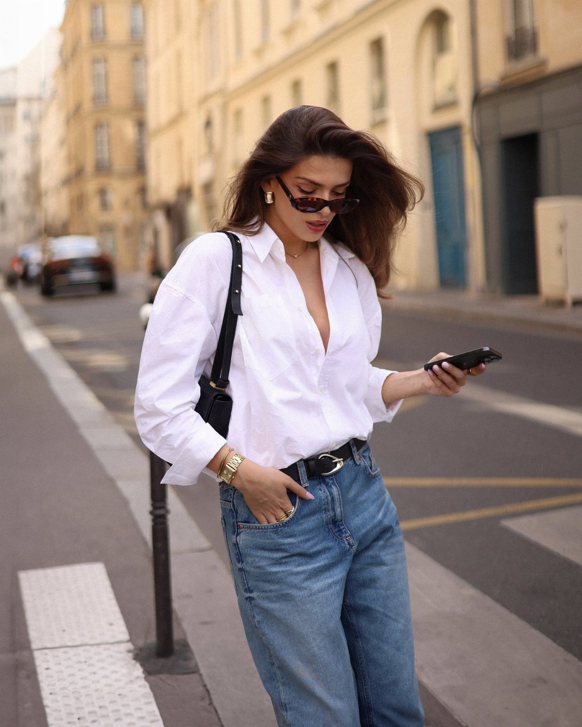 Woman in a white button-down shirt and blue jeans on a city street.