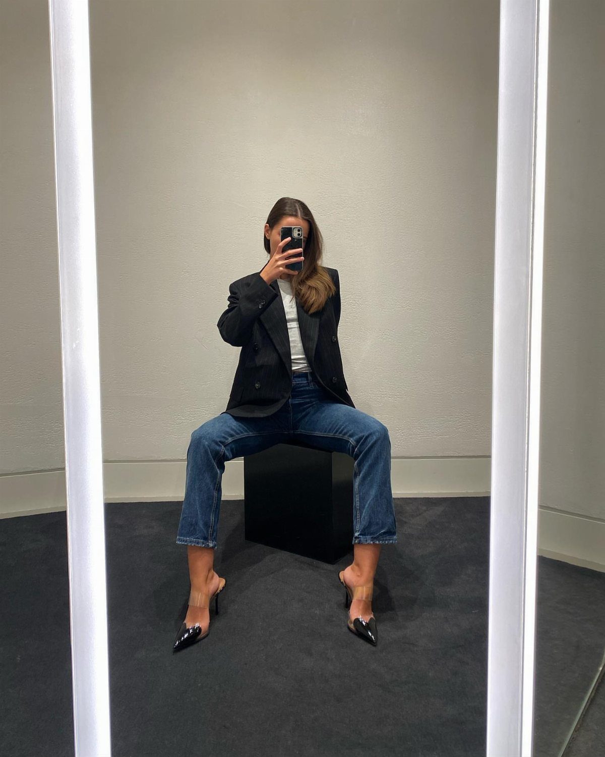 Woman in black blazer and blue jeans wearing black pointed-toe high heels.