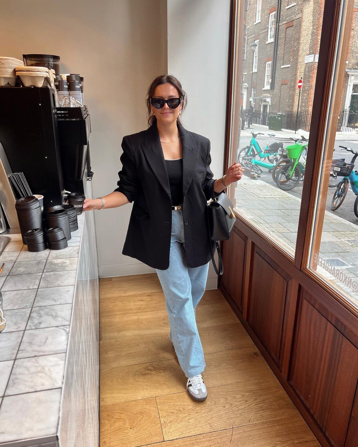 Woman in black blazer and light blue jeans posing indoors by a window