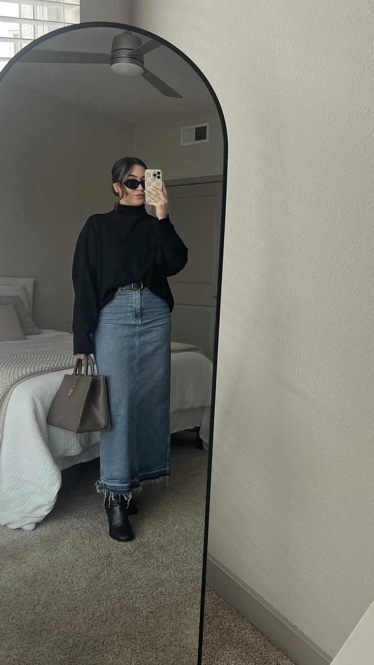 Woman in black turtleneck and long denim skirt posing for a mirror selfie.