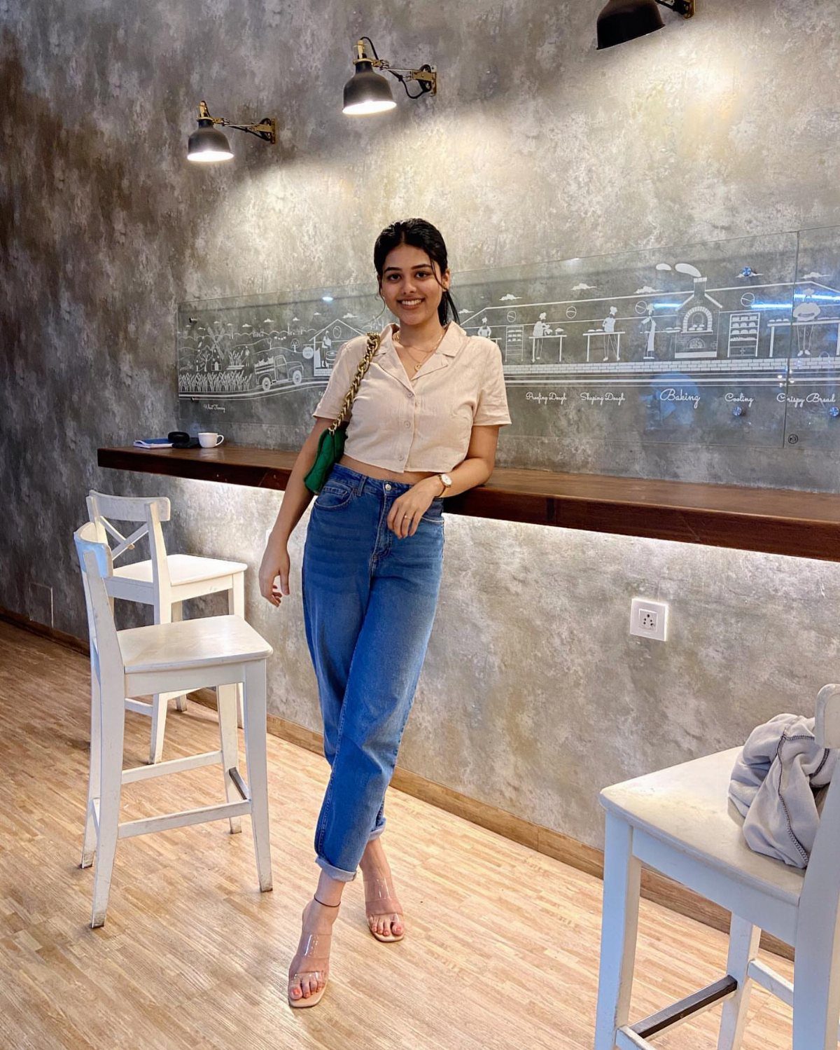 Woman in beige button-down crop top and blue jeans leaning on a bar counter