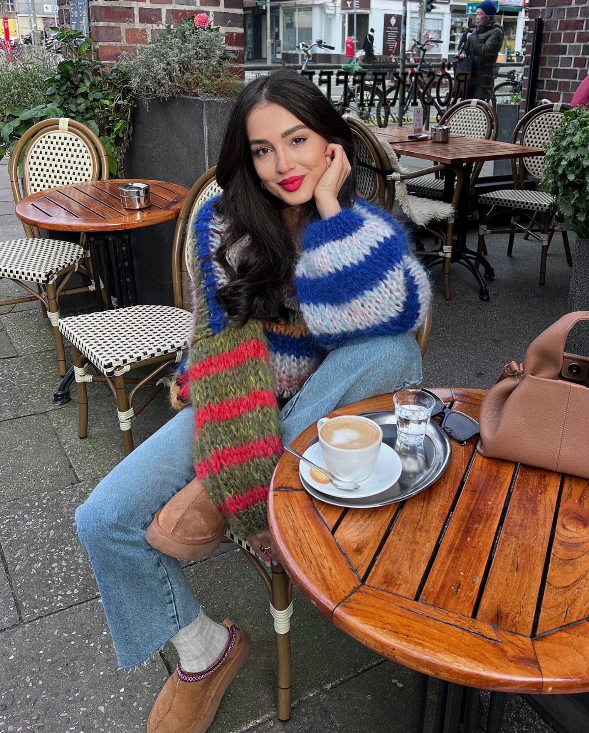 Woman in a colorful striped sweater and blue jeans sitting at a cafe table.