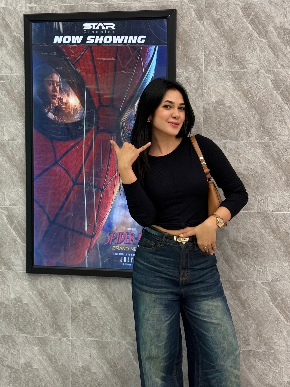 Woman in black top and blue jeans posing by a movie poster.