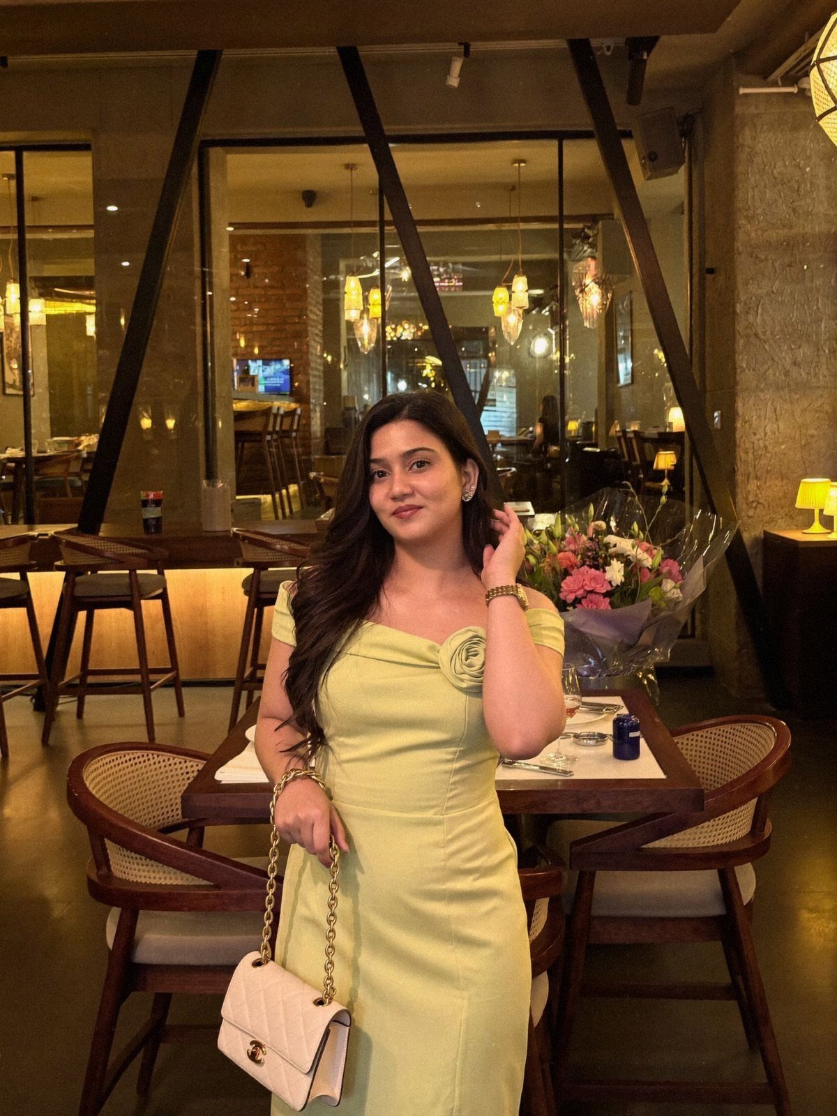 Woman in a light yellow summer dress holding a white handbag in a restaurant