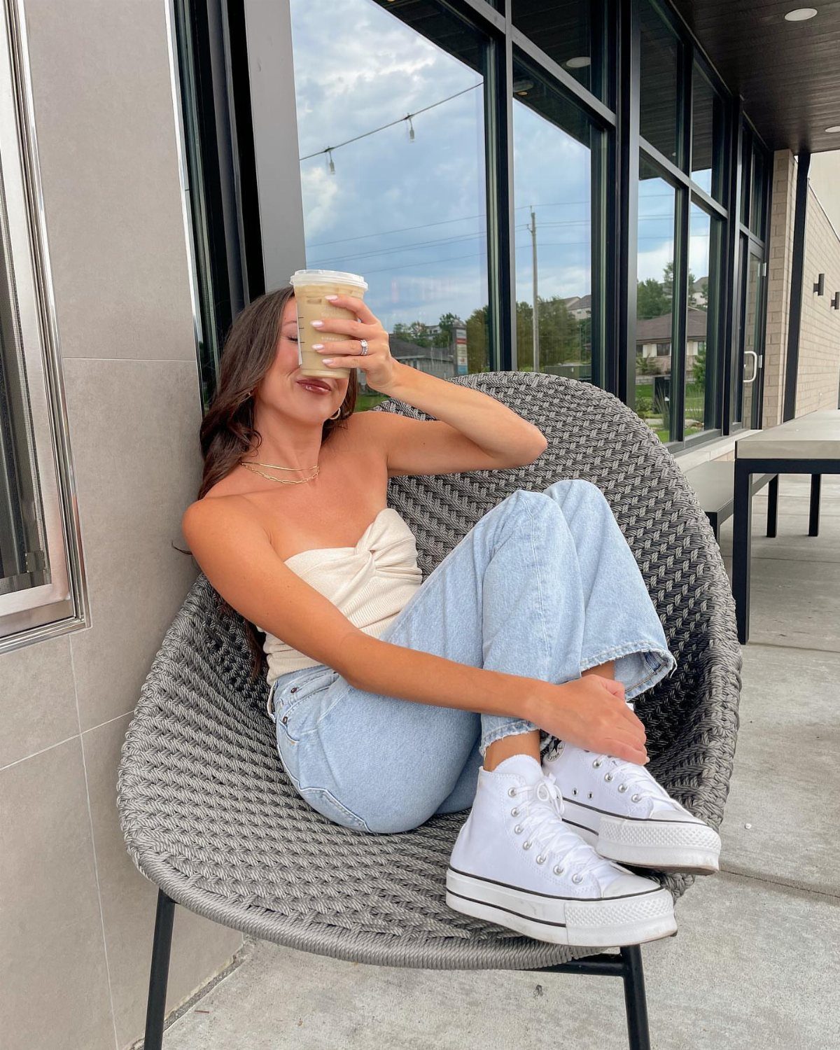 Woman in white tube top and light blue jeans sitting in woven chair